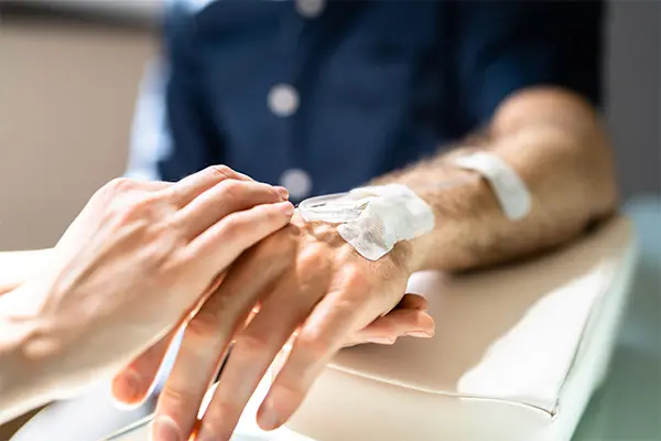 Image shows a close-up shot of an oncology nurse's hands placing tape on a patient's intravenous infusion line. The line resembles those used for immunotherapy treatments.